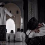 Seorang santri duduk tertunduk dalam suasana muram di lorong pesantren, menggambarkan kesedihan dan tekanan batin akibat kasus yang mengguncang lembaga pendidikan agama.