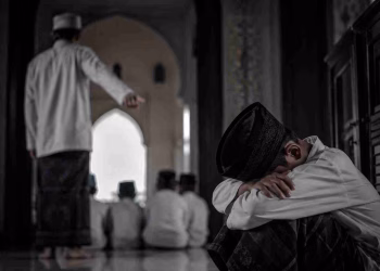 Seorang santri duduk tertunduk dalam suasana muram di lorong pesantren, menggambarkan kesedihan dan tekanan batin akibat kasus yang mengguncang lembaga pendidikan agama.
